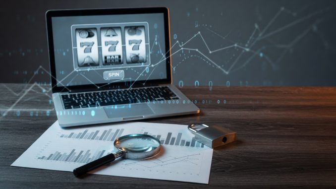 Moody blue-lit photo of a laptop showing slot reels, with a magnifying glass over