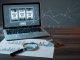 Moody blue-lit photo of a laptop showing slot reels, with a magnifying glass over