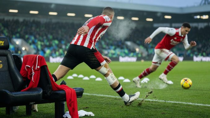 Pitch-level photo under floodlights: empty bench seat with a red bib hinting at a