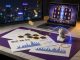Photo of a modern desk with a laptop showing a blurred Greek-myth slot, coins